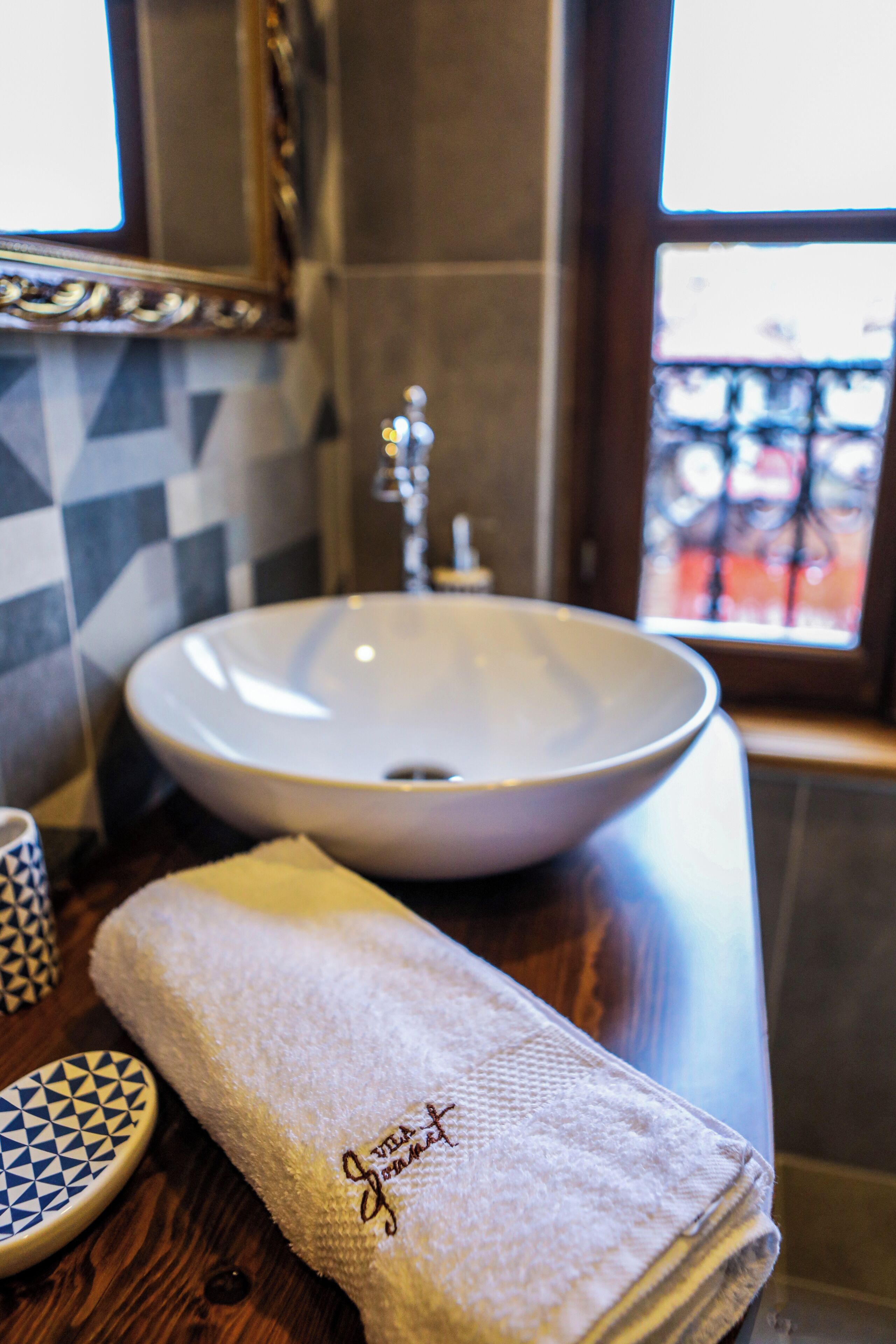 A bathroom with a white sink, a towel with embroidered text, and a patterned dish.