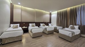 A hotel room with four single beds arranged in a row, a wooden headboard, a large mirror, and a curtain-covered window. - Al Jabri Hotel (Makkah)