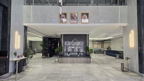A modern lobby with a marble floor, a reception desk, framed portraits above the desk, and a sign with Arabic text. - Al Jabri Hotel (Makkah)