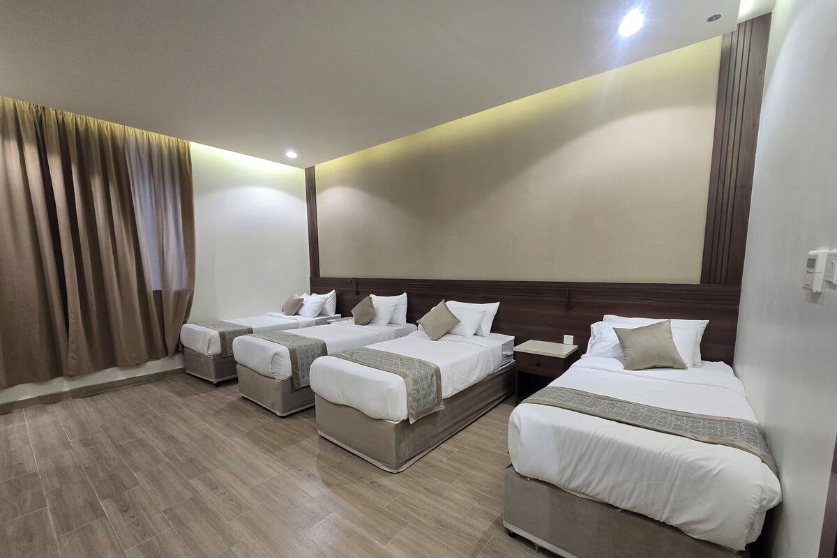 A hotel room with four single beds, a wooden floor, and a large window with curtains.