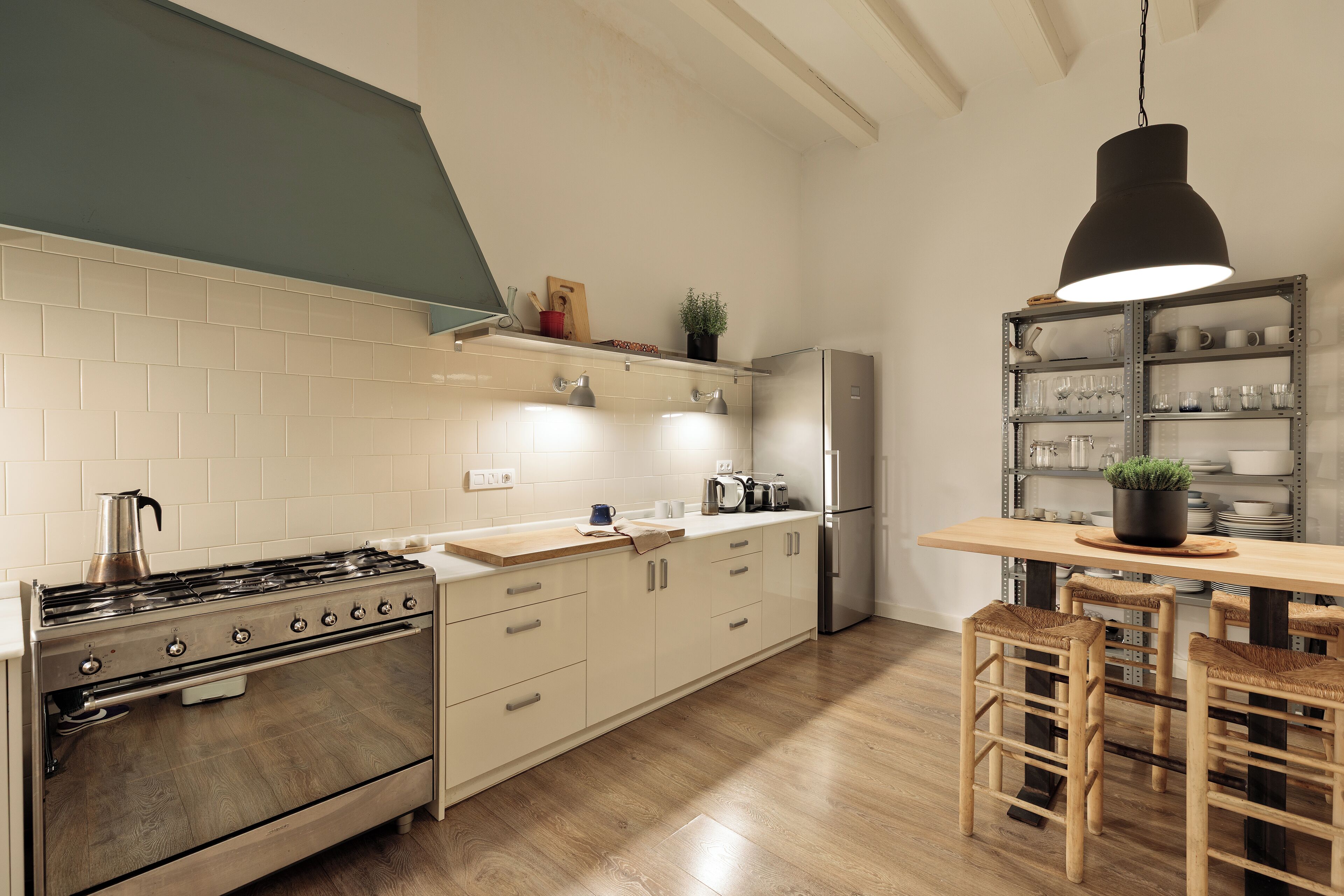 A modern kitchen with a stainless steel stove, wooden bar stools, and a hanging pendant light.