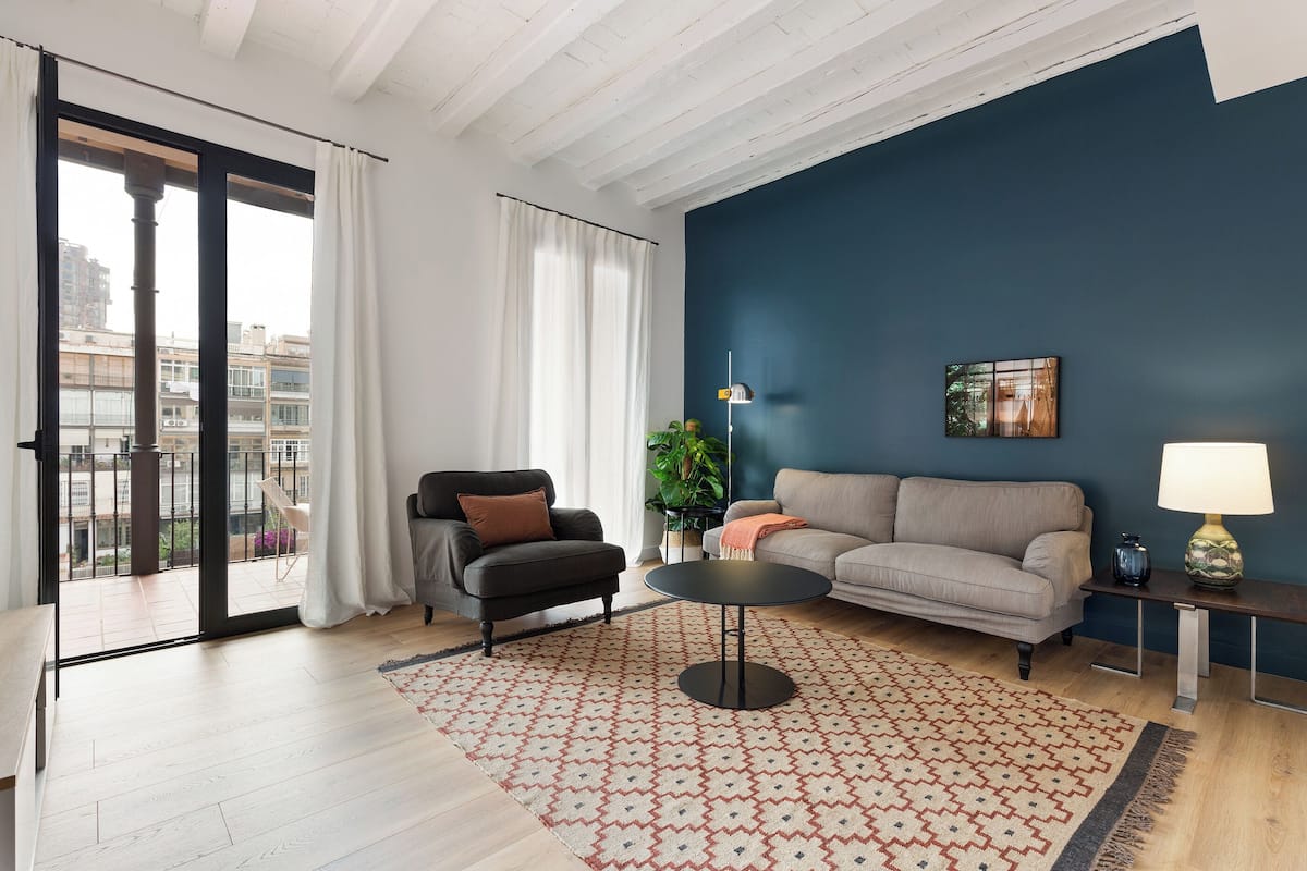 Una sala de estar moderna con un ventanal grande, un sofá, un sillón, una mesita redonda y una lámpara.