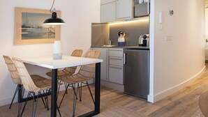 Una cocina moderna con armarios blancos, un refrigerador de acero inoxidable y un comedor con mesa blanca y sillas de mimbre.