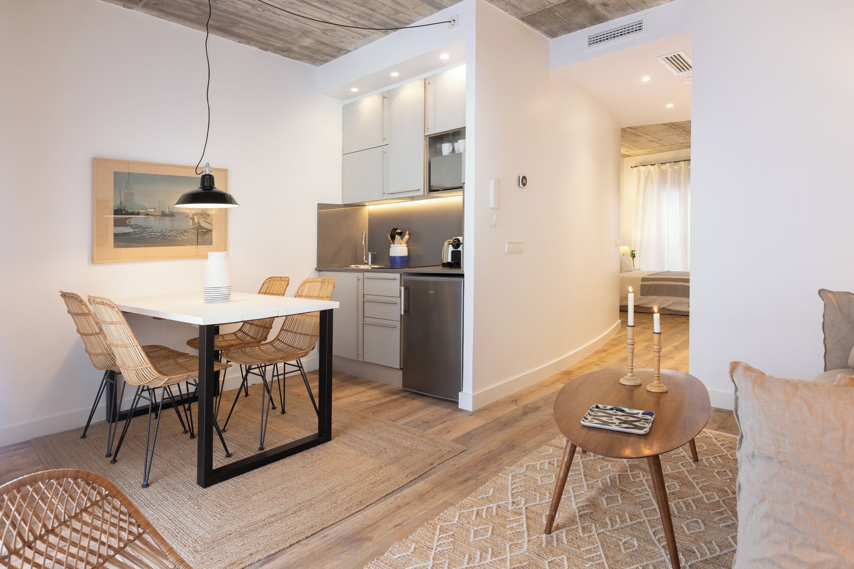 A modern kitchen with white cabinets, a built-in oven, and a dining area with a white table and wicker chairs.