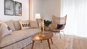 Una sala de estar con un sofá color beige, una mesa de centro de madera con velas, un sillón de mimbre y dos cuadros en la pared.