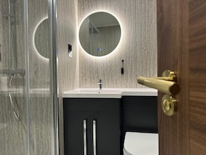 A modern bathroom with a glass shower enclosure, a round mirror, and a white sink. - Marian Resort And Spa  (Rhyl)