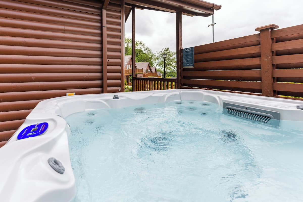 Ein Whirlpool mit Bedienfeld, umgeben von einem Holzzaun und einem überdachten Bereich.