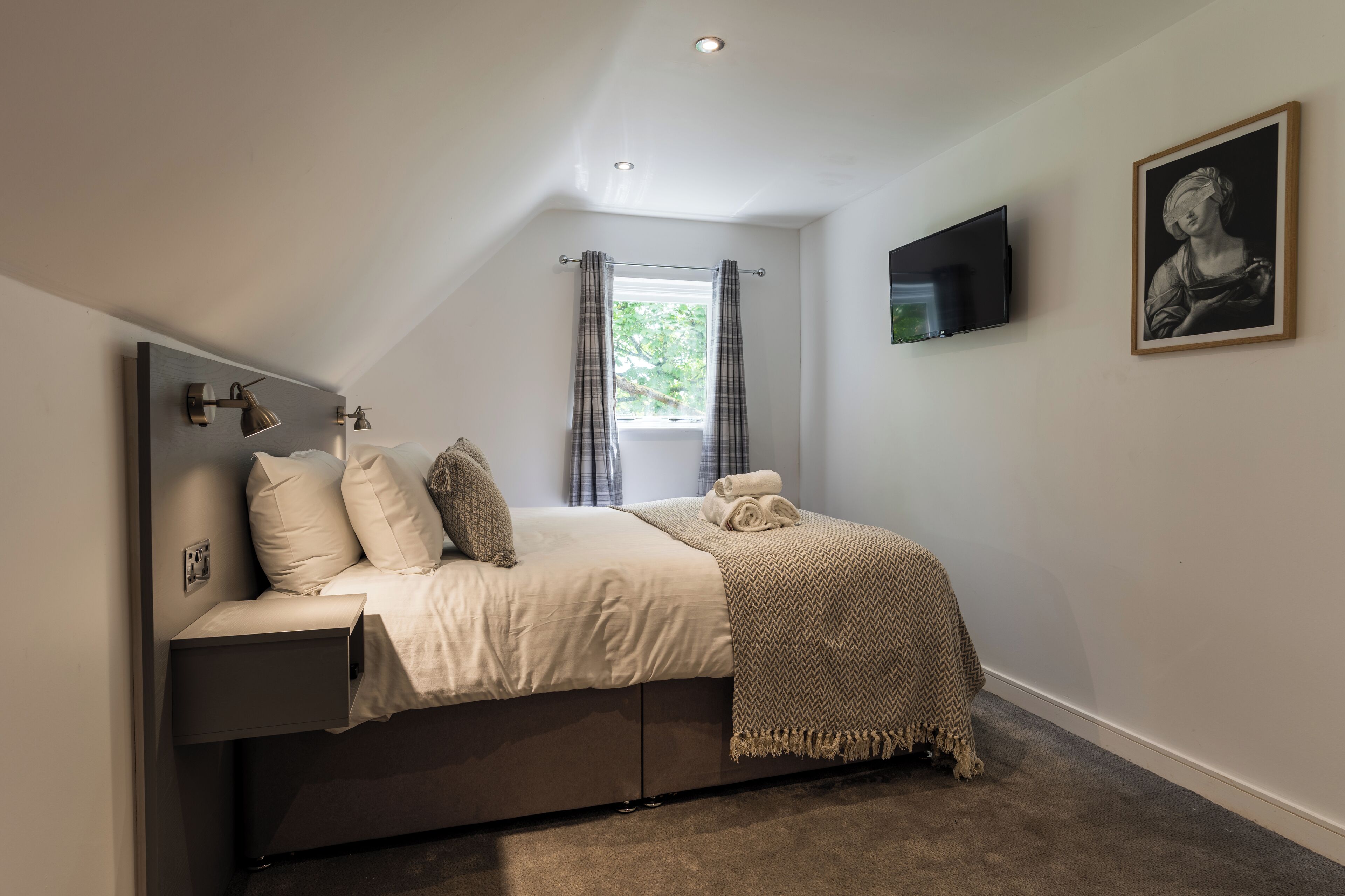 A bedroom with a bed, a TV, a painting, and a window with curtains.
