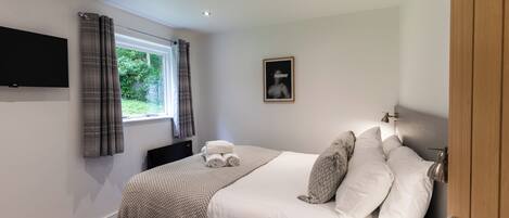 A bedroom with a bed, a flat-screen TV mounted on the wall, a window with curtains, and a framed picture on the wall.
