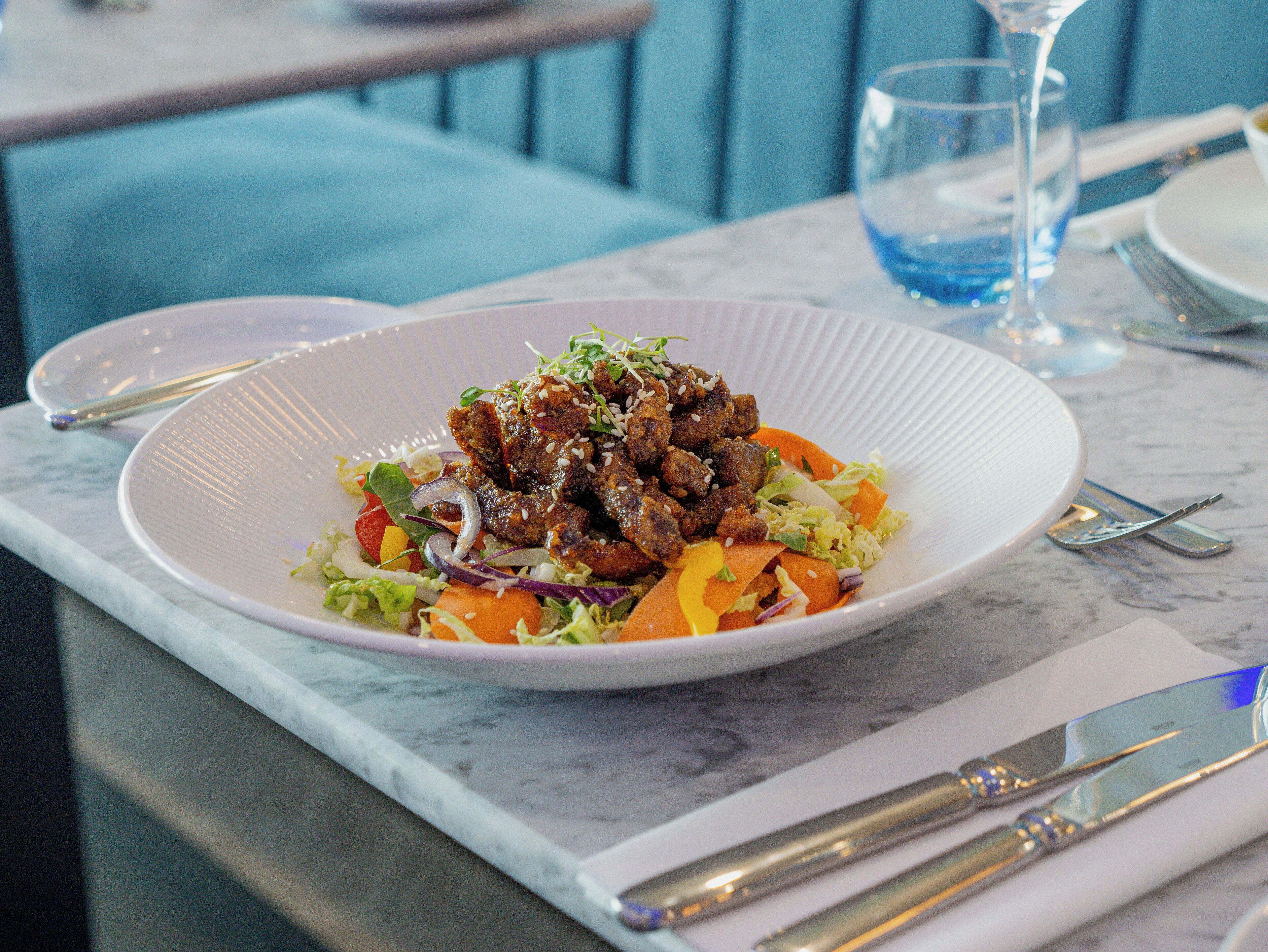 A white plate with a dish of food, a fork, and a knife on a marble table.
