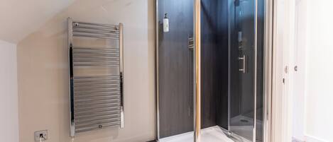 Un baño moderno con cabina de ducha de vidrio, toallero empotrado y un enchufe visible.
