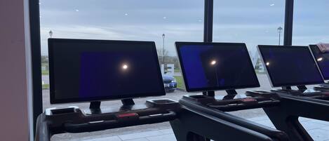 A row of computer monitors in a room with large windows.