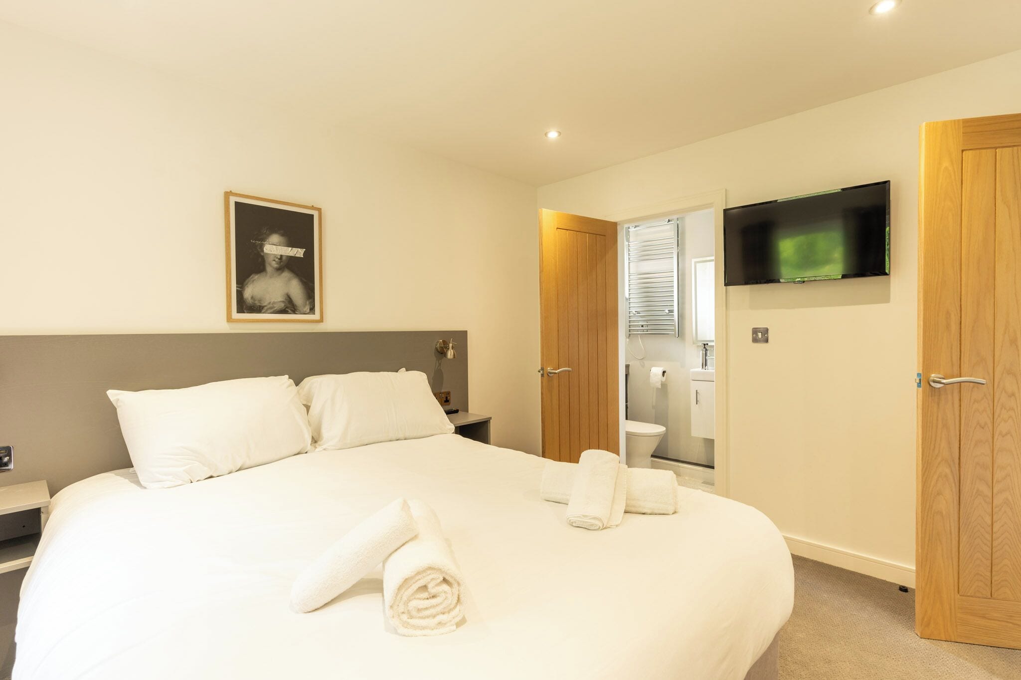 Une chambre d’hôtel avec un grand lit, un téléviseur à écran plat fixé au mur et une armoire en bois.