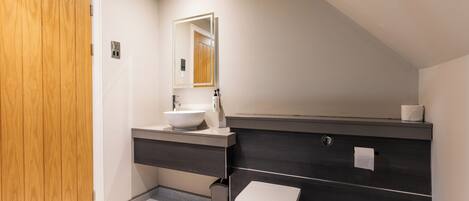 Et moderne badeværelse med en trædør, en hvid vask, et mørkt underskab og et hvidt toilet.