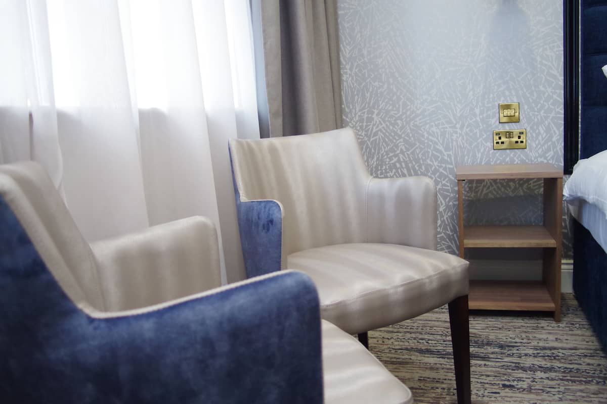 Ein Hotelzimmer mit zwei Sesseln, einem Nachttisch aus Holz und einem Bett.
