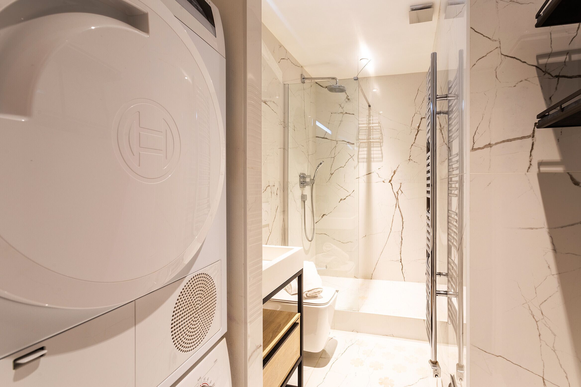 A modern bathroom with a glass-enclosed shower, a white toilet, and a built-in washing machine.