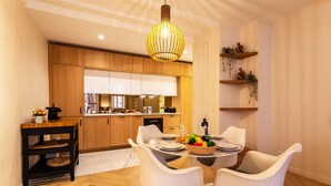 A modern kitchen with wooden cabinets, a dining area with white chairs, and a hanging light fixture.
