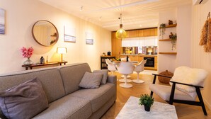 A modern living room with a grey sofa, a round mirror, and a dining area with white chairs and a hanging light fixture.
