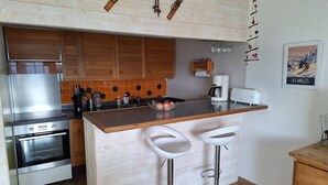 A kitchen with wooden cabinets, a stainless steel oven, a coffee maker, and two bar stools.