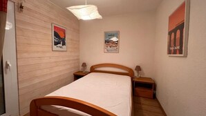 A bedroom with a wooden bed, two bedside tables, a hanging light fixture, and three posters on the wall.