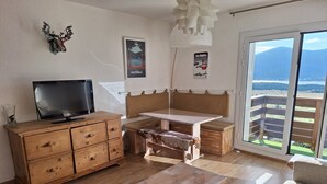 A cozy living room with a wooden TV stand, a bench, and a table. There are posters on the wall and a view of the outdoors through a sliding door.