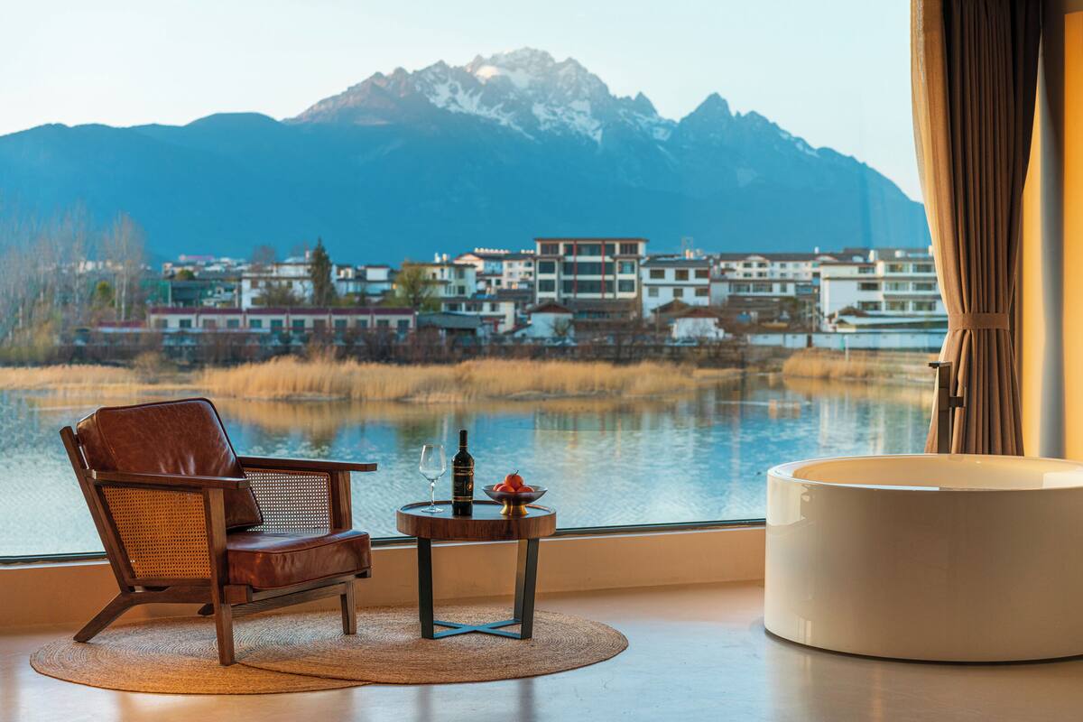Ein Zimmer mit Bergblick, ein Sessel, ein kleiner Tisch mit Flasche und Glas sowie ein runder Hocker.