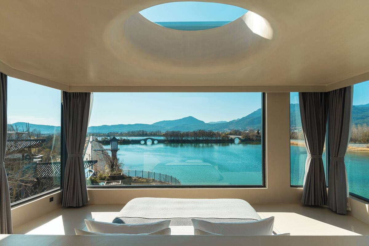 Ein modernes Hotelzimmer mit einem großen Bett, einem Oberlicht und Blick auf einen Fluss und Berge.