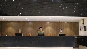A reception desk with three staff members, wooden paneling on the walls, and a marble countertop. - MagTree Genting Highlands (Genting Highlands)