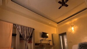 Une chambre d’hôtel comprenant un lit, une petite table, un canapé, un ventilateur de plafond, une télévision et un luminaire fixé au mur.