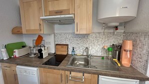 A compact kitchen with wooden cabinets, a built-in oven, a sink, and a coffee maker.