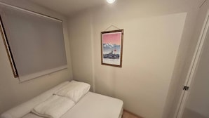 A bedroom with a single bed, a window with blinds, a framed picture on the wall, and a door.