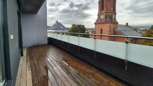 A balcony with a wooden floor and a view of a church with a clock tower. - Modern Room in Apartment With Private Balcony in Beutiful Oslo  (Oslo)