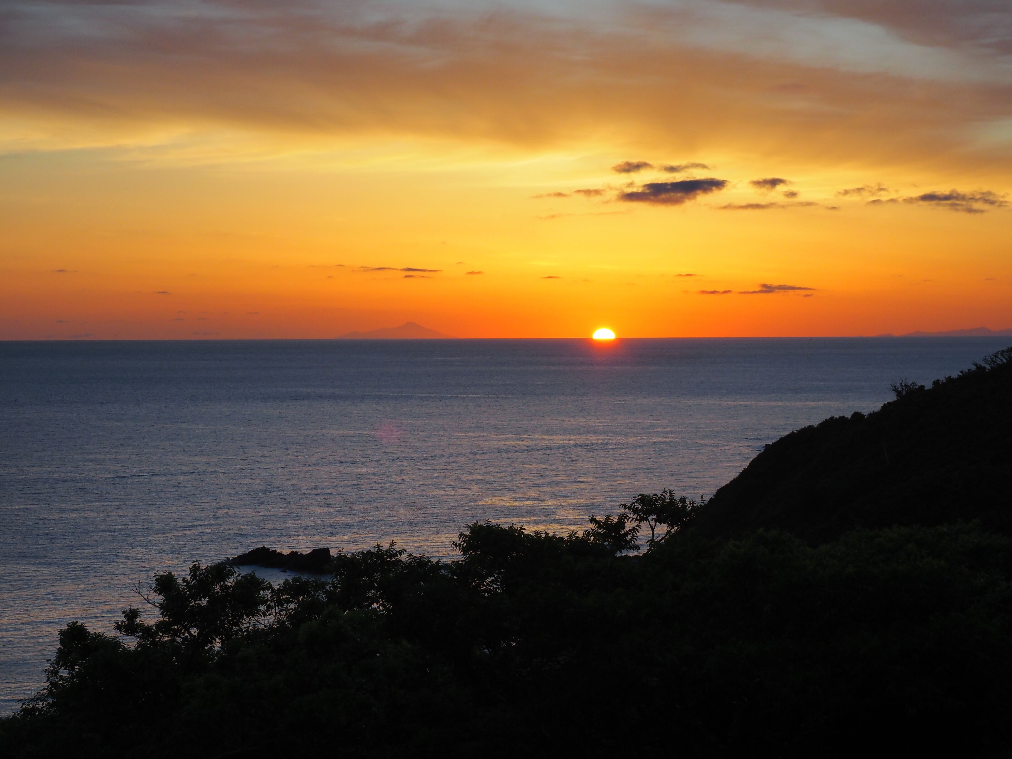 Ein Sonnenuntergang über dem Meer mit der Silhouette einer Küstenlinie im Vordergrund.
