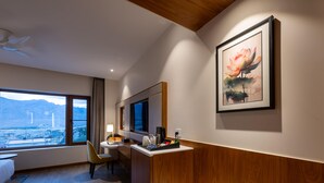 Una habitación de hotel con una cama, un escritorio con una silla, una ventana con vistas a montañas y una obra de arte enmarcada en la pared.