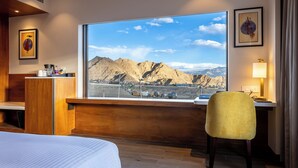 Habitación de hotel con una ventana grande que ofrece vistas a la montaña, una cama, un escritorio y una silla.