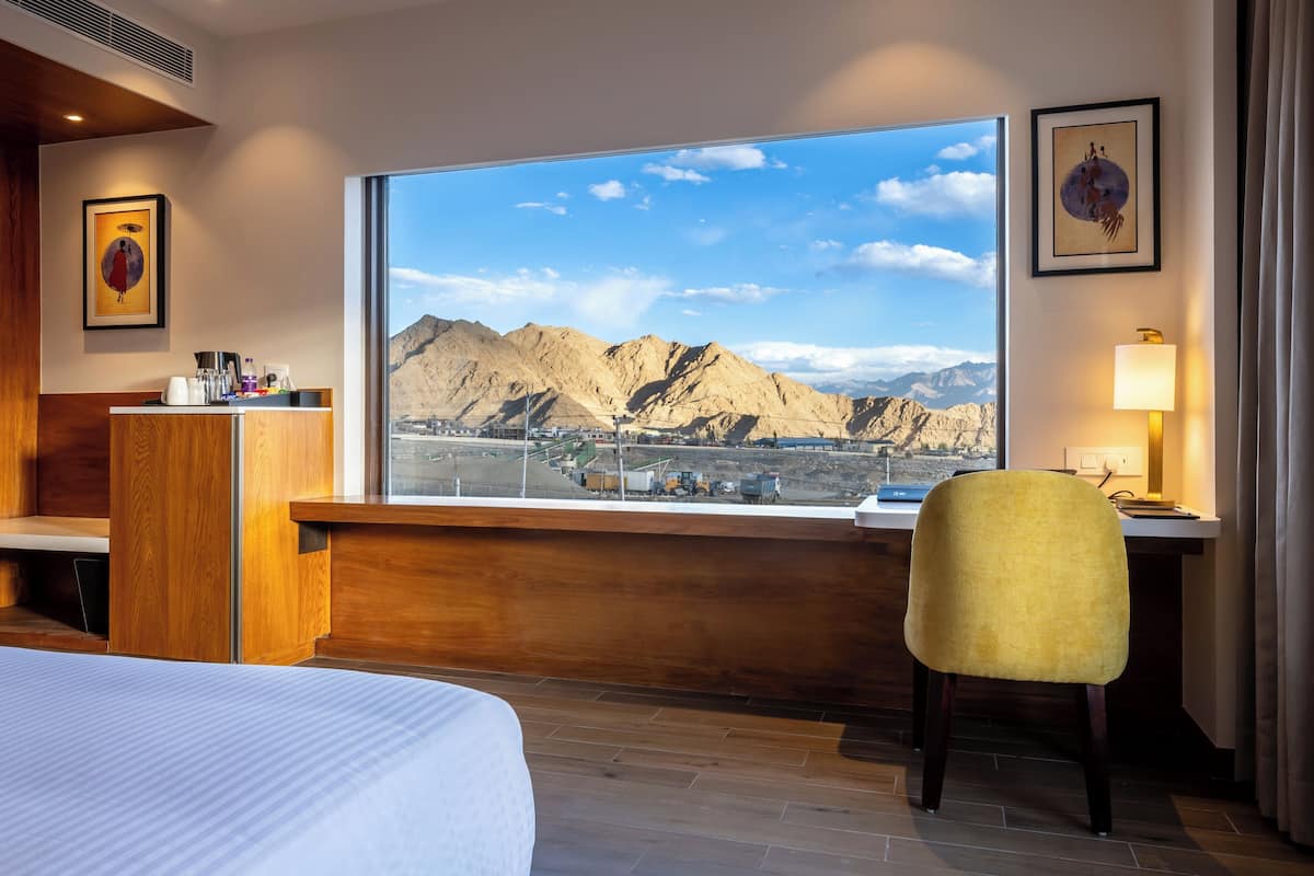 A hotel room with a large window offering a mountain view, a bed, a desk, and a chair.