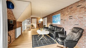 Ein modernes Wohnzimmer mit Backsteinwand, Holzboden, schwarzem Ledersofa und einem runden Couchtisch.