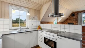 Eine moderne Küche mit weißen Schränken, einer Edelstahl-Dunstabzugshaube, einem eingebauten Ofen und einem Fenster mit Blick ins Freie.