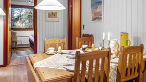 A dining area with a wooden table, chairs, a white pendant light, and a framed picture on the wall.