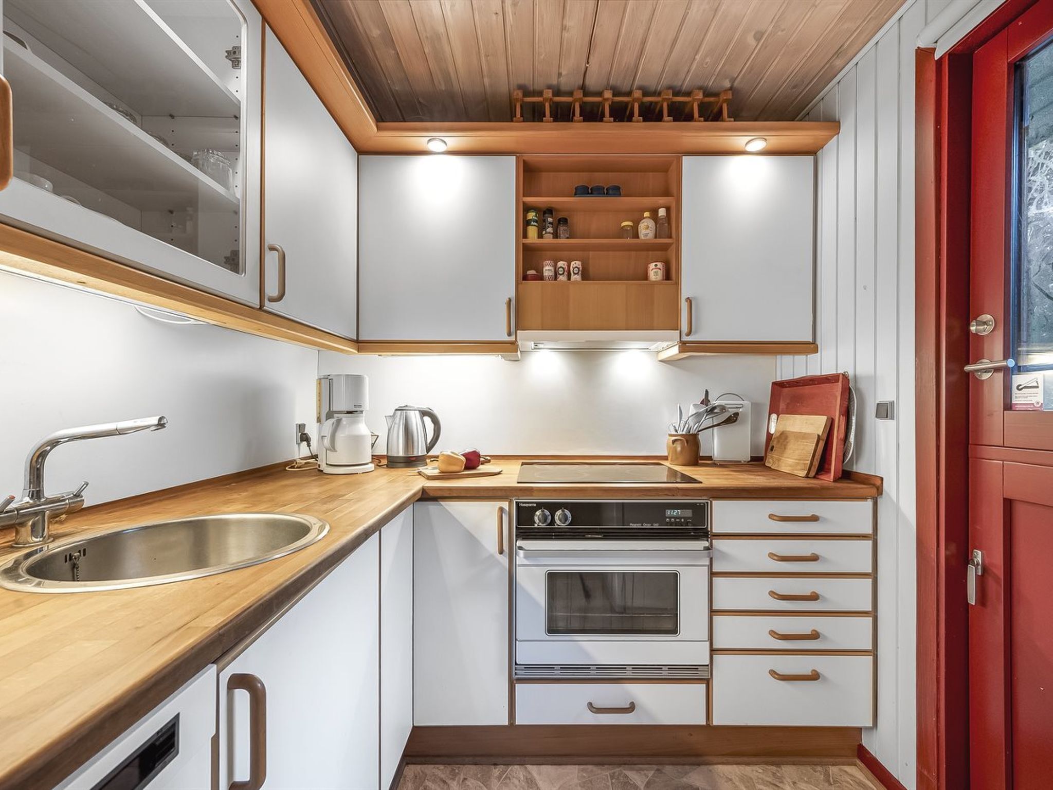 Een kleine keuken met witte kasten, een roestvrijstalen spoelbak, een ingebouwde oven en een houten aanrecht.