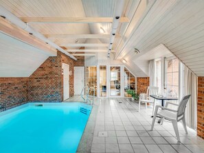Une piscine intérieure dotée d’un sol carrelé, d’un mur en briques et d’un plafond avec des poutres en bois.