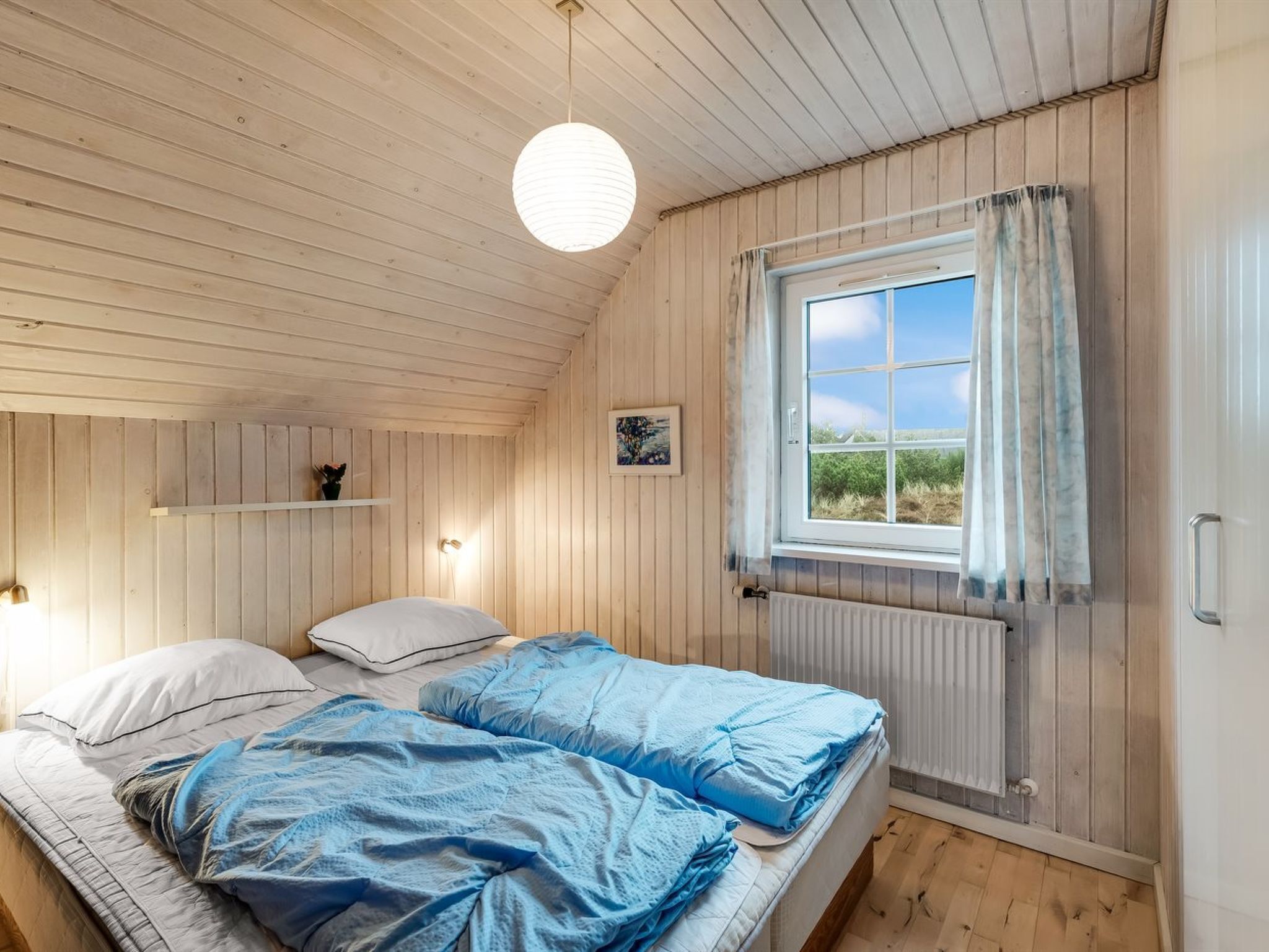 Ein Schlafzimmer mit zwei Betten, einem Fenster mit Vorhängen, einer Pendelleuchte und einer Heizung.
