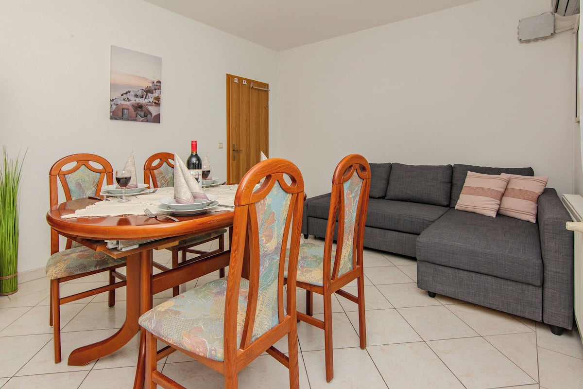 A dining area with a wooden table and chairs, a gray sofa, and a door in the background.