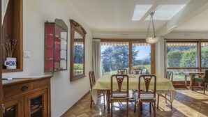 A dining area with a table set for four, surrounded by chairs, a cabinet with glass doors, and a large window offering a view of greenery. - The Balcony of Sainte-Anne, Lake View (Annecy-le-Vieux)