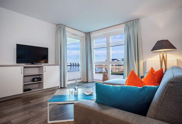 Una sala de estar moderna con un televisor de pantalla plana, un sofá con cojines azules y naranjas, una mesa de centro y una lámpara.