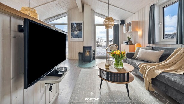 Ein modernes Wohnzimmer mit einem großen Flachbildfernseher, einer Couch, einem Couchtisch mit Blumenvase und einem Kamin.