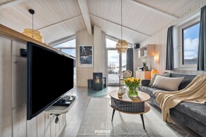 Ein modernes Wohnzimmer mit einem großen Flachbildfernseher, einer Couch, einem Couchtisch mit Blumenvase und einem Kamin.