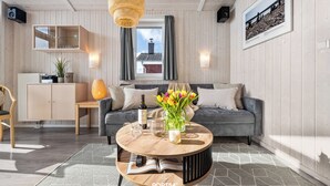 Ein modernes Wohnzimmer mit einem runden Couchtisch, einer Couch, einem Bücherregal und einem Fenster mit Vorhängen.
