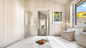 Ein Schlafzimmer mit Holzwänden, einem Bett mit Steppdecke, zwei Kissen, einem gerahmten Bild und einem Fenster mit Blick auf ein Gebäude.