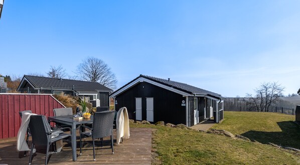 Eine Holzterrasse mit Gartenmöbeln, ein schwarzes Gebäude mit weißem Zierrat und ein roter Zaun.